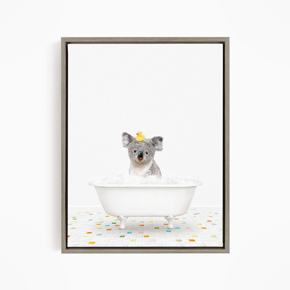 A koala bear sitting in a white bathtub filled with bubbles, with a rubber duck on its head.