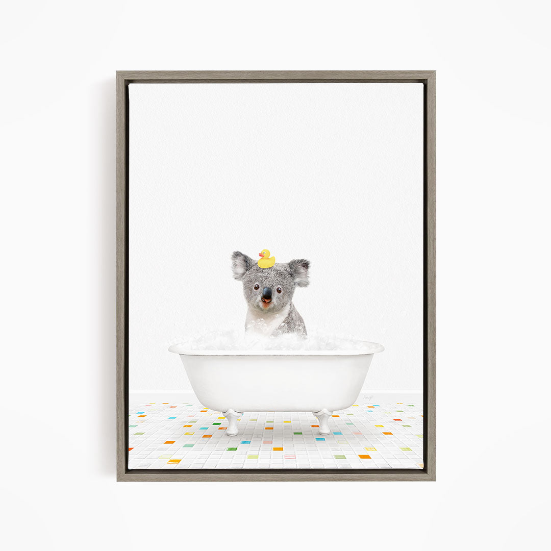 A koala bear sitting in a white bathtub filled with bubbles, with a rubber duck on its head.