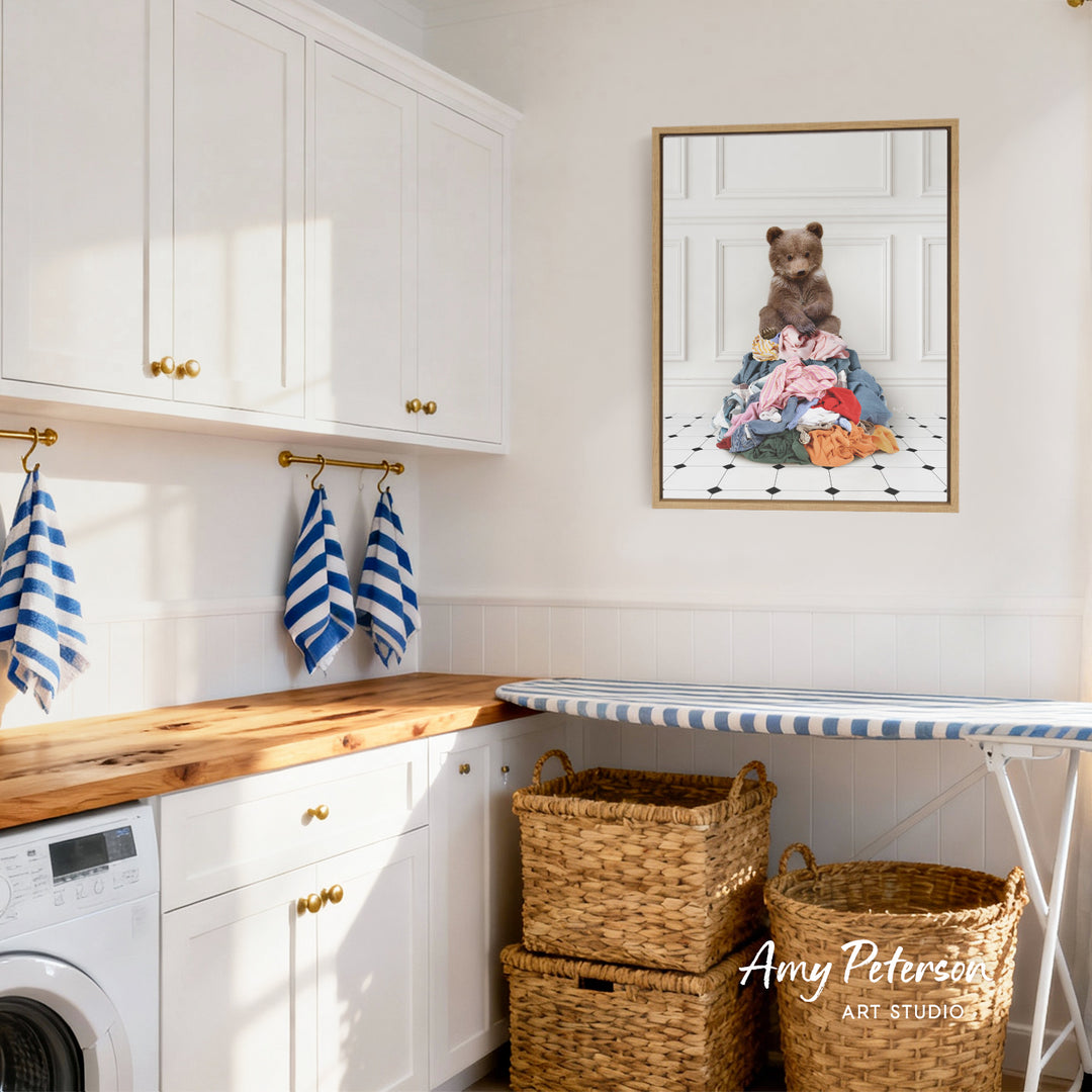 A cozy laundry room with white cabinets, a wooden countertop, and a framed photo of a teddy bear sitting on a pile of clothes.