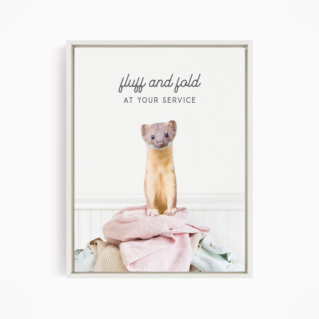 A small brown and white ferret sitting on a pile of clothes, with the text "fluff and fold at your service" written above the image.