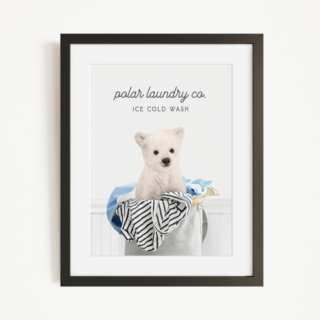 A framed image of a white dog sitting in a laundry basket filled with clothes, with the text "polar laundry co. ICE COLD WASH" displayed above the dog.
