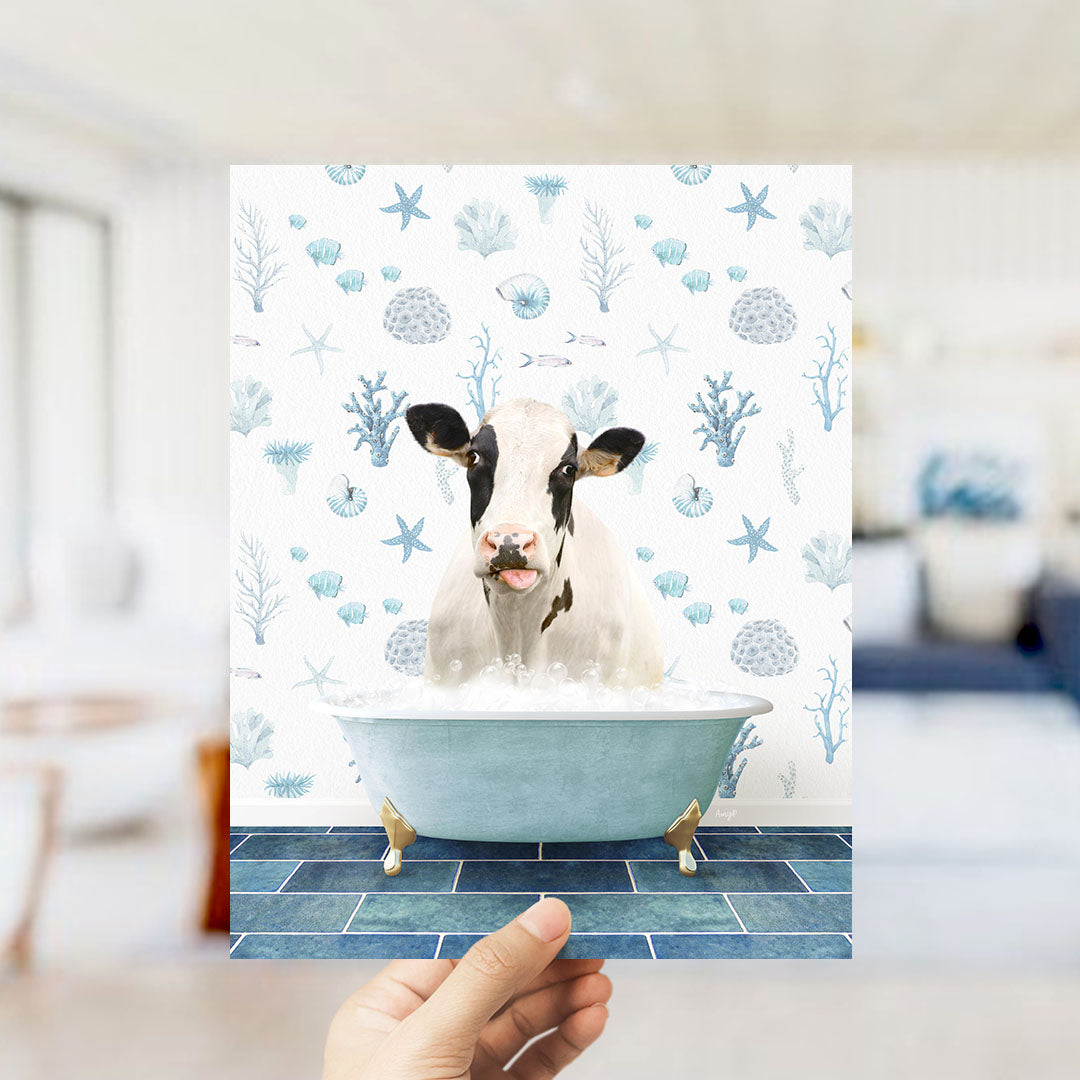 A hand is holding up a picture of a cow sitting in a bathtub filled with bubbles, surrounded by a blue and white ocean-themed background.