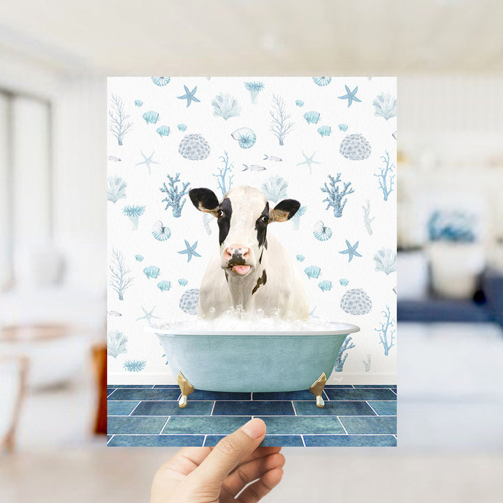 A hand is holding up a picture of a cow sitting in a bathtub filled with bubbles, surrounded by a blue and white ocean-themed background.