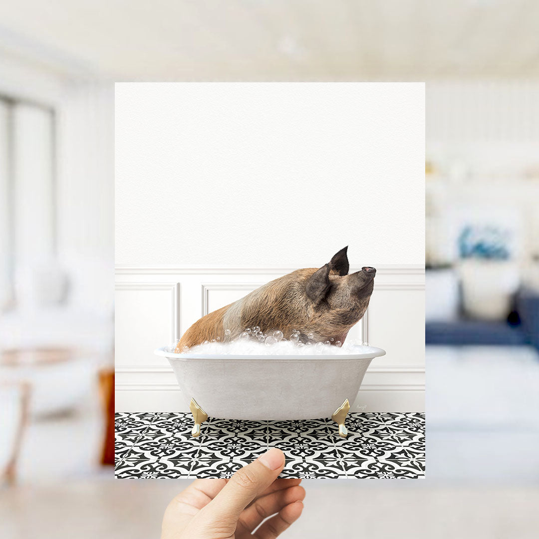 A brown pig sitting in a white bathtub filled with bubbles, with a hand holding the photo up to the camera.