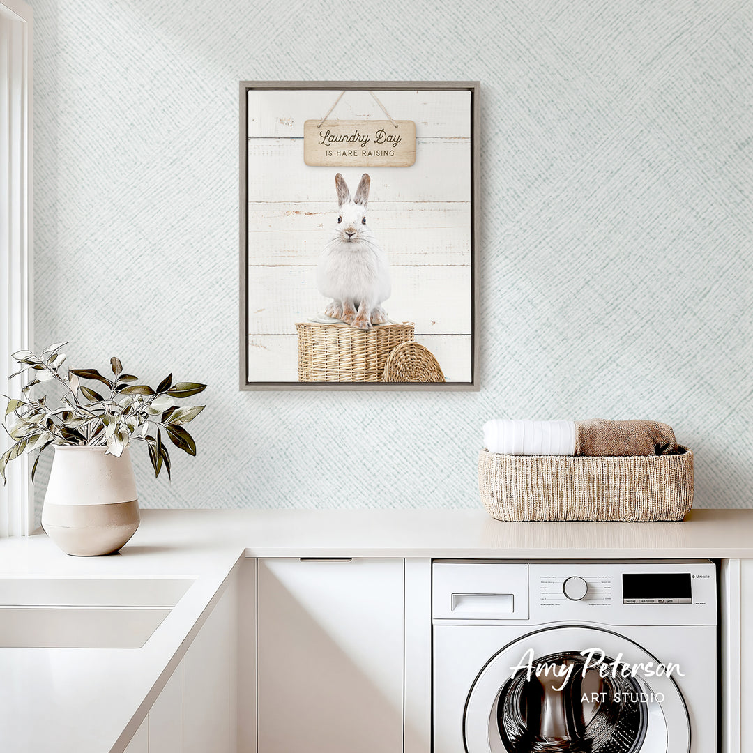 a laundry room with a framed picture of a rabbit sitting on a wicker basket, a potted plant, and a basket of towels on a counter.