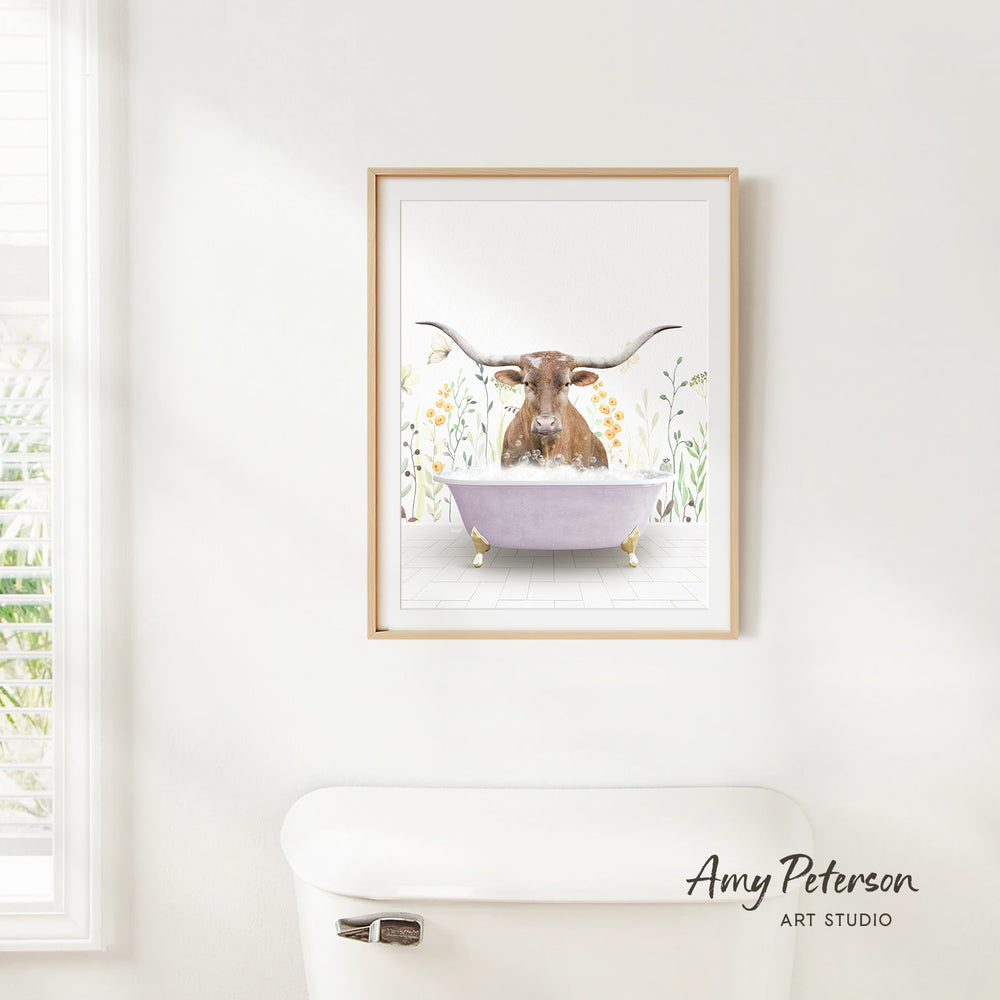 A framed print of a bull with horns sitting in a bathtub, surrounded by flowers, is hanging on a white wall.