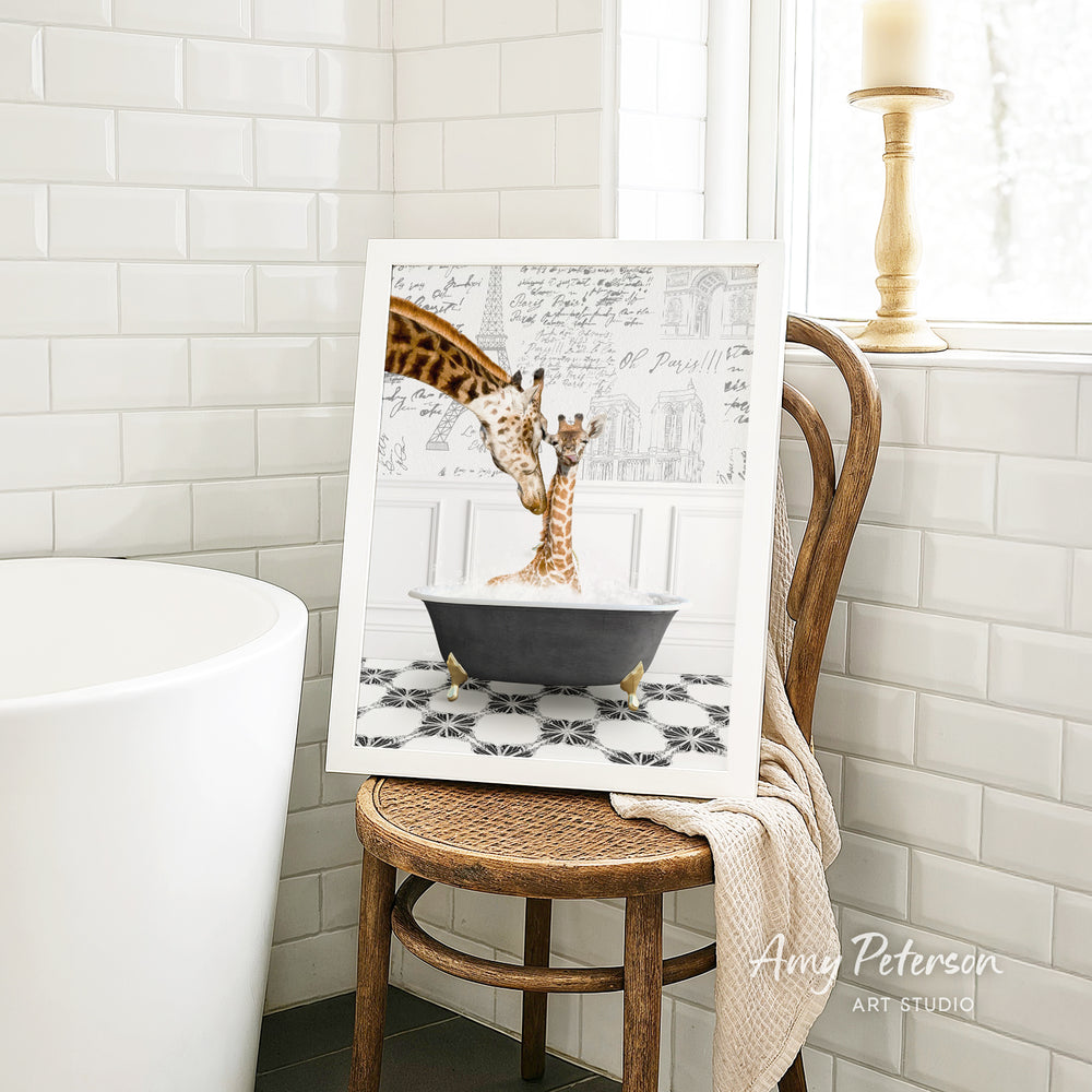 A framed image of two giraffes sitting in a bathtub, with one giraffe appearing to be bathing the other. The image is displayed on a wooden chair in a bathroom setting.