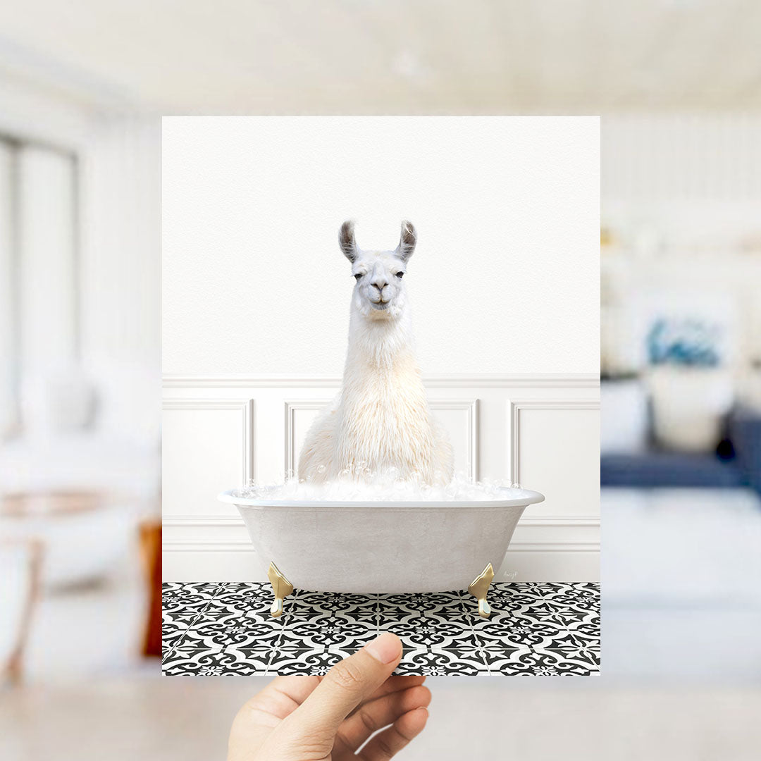 A white llama sitting in a white bathtub filled with bubbles, with a hand holding the image up to the viewer.
