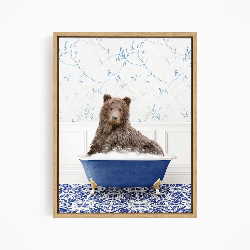 A brown bear sitting in a blue bathtub filled with bubbles, with a blue and white floral patterned wall behind it.