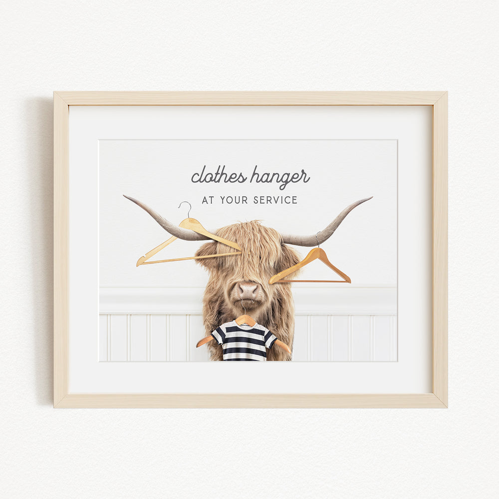 A framed image depicting a large, furry animal with a pair of clothes hangers attached to its head, accompanied by the text "clothes hanger at your service".