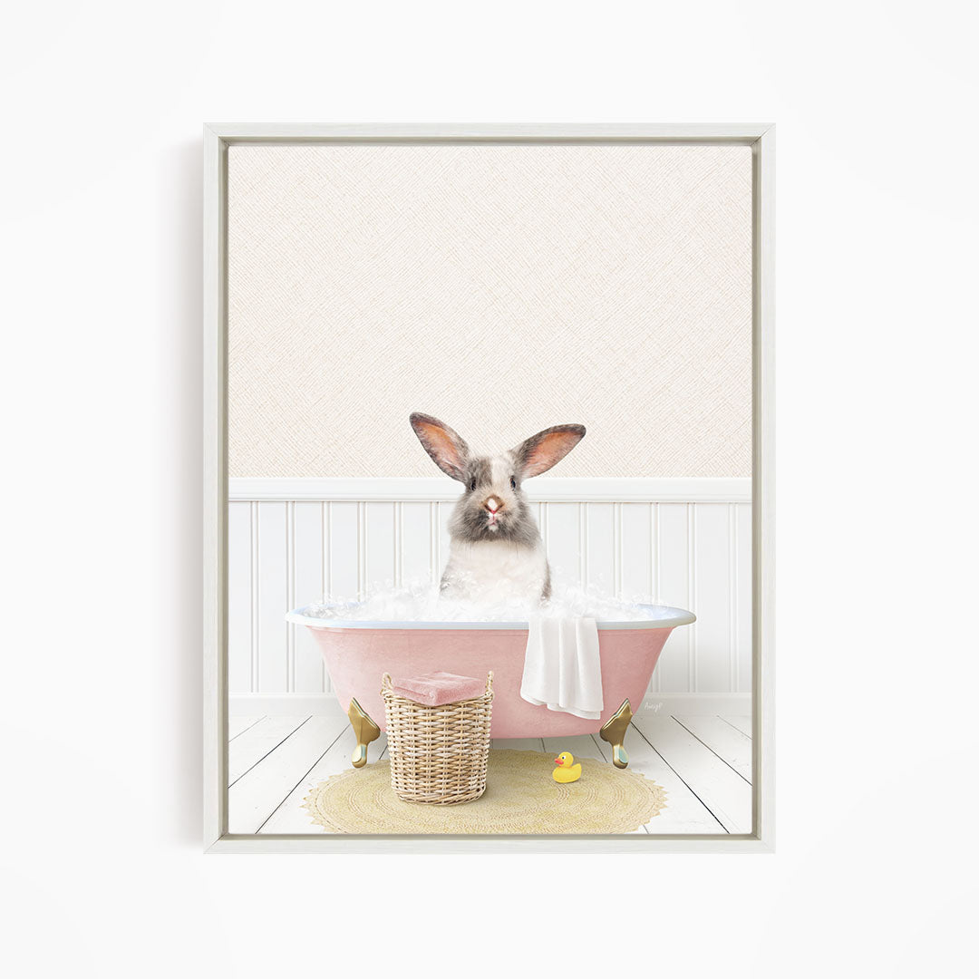 A white rabbit sitting in a pink bathtub filled with bubbles, surrounded by a yellow rubber duck and a wicker basket.