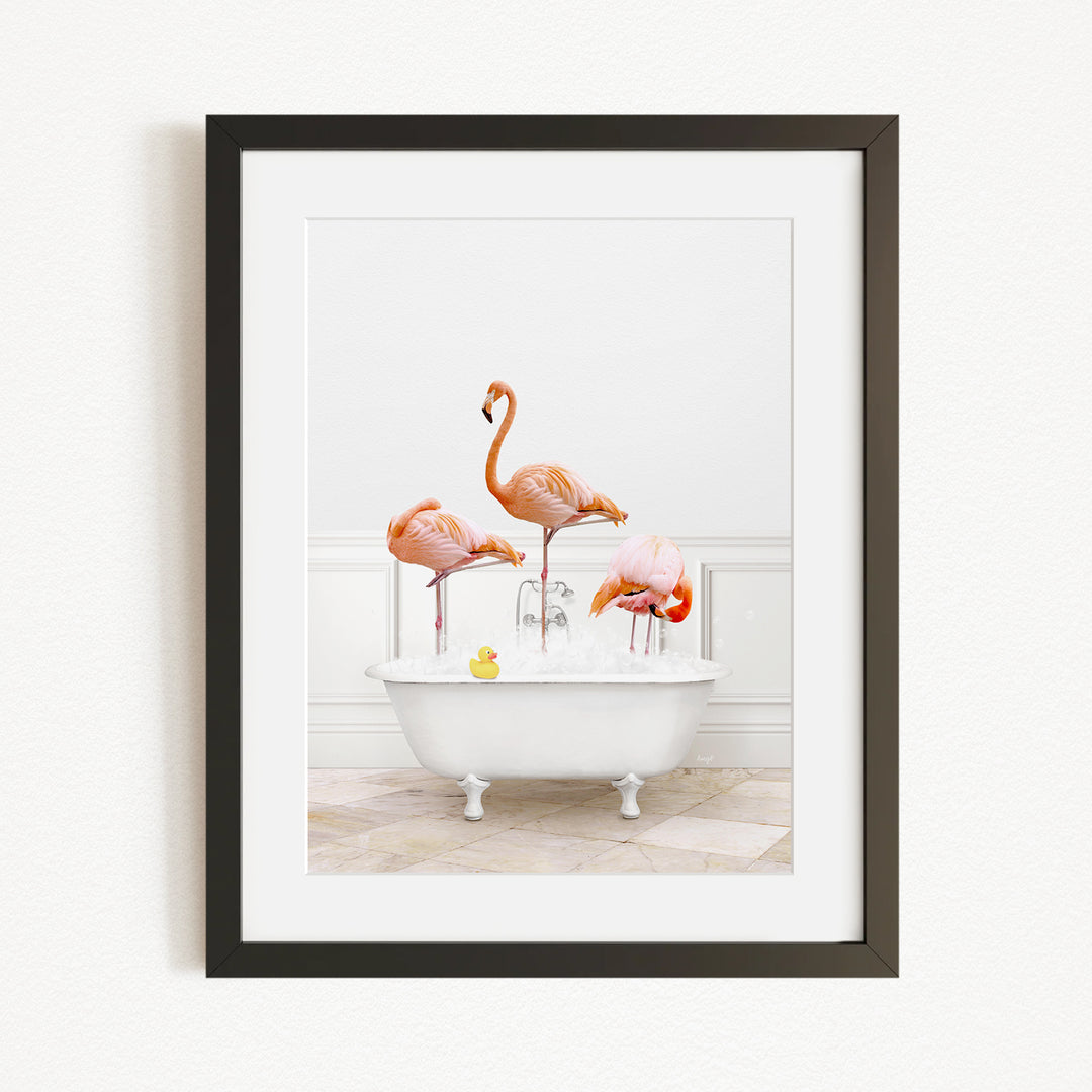 A framed image depicting three flamingos standing in a white bathtub filled with water, with a yellow rubber duck floating in the water.