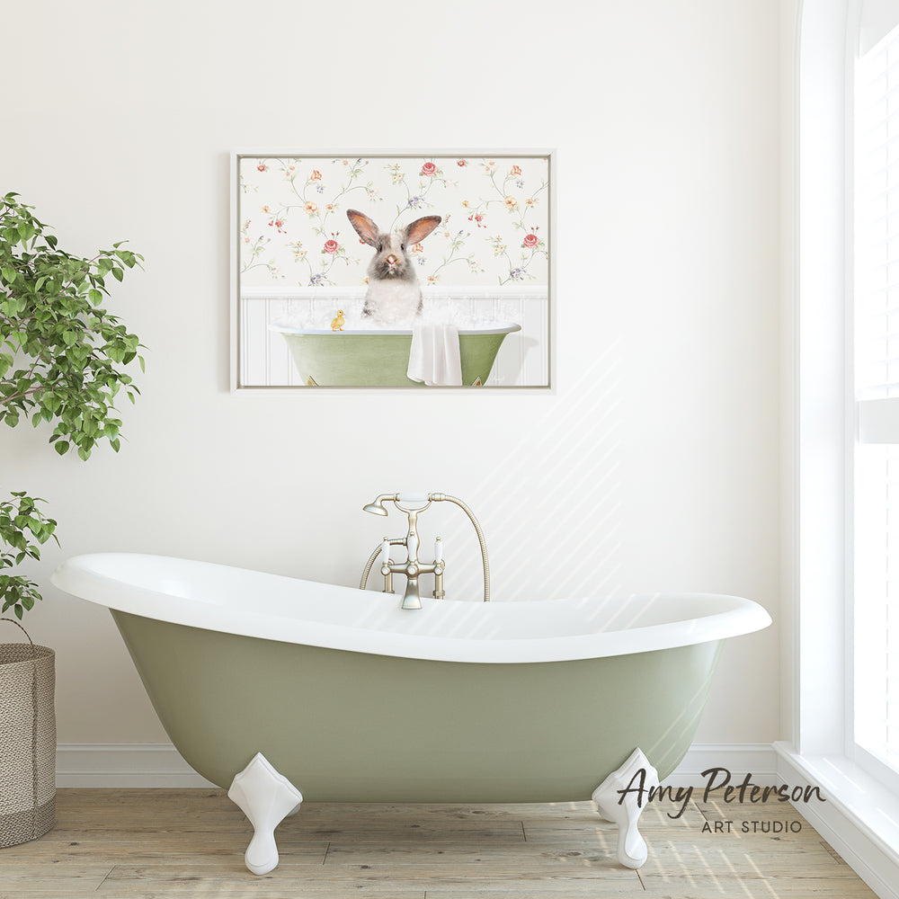 A green clawfoot bathtub with a white interior sits in a bright, white bathroom. Above the bathtub, a framed image of a rabbit sitting in a bathtub is displayed on the wall.