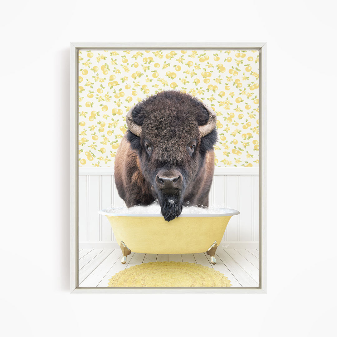 A buffalo with a black mane and horns is sitting in a yellow bathtub, with a yellow and white floral patterned wall behind it.