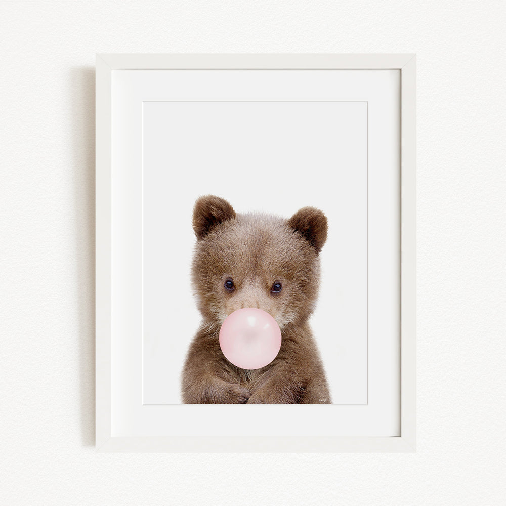 A cute brown bear is blowing a bubble with a pink bubble gum bubble.