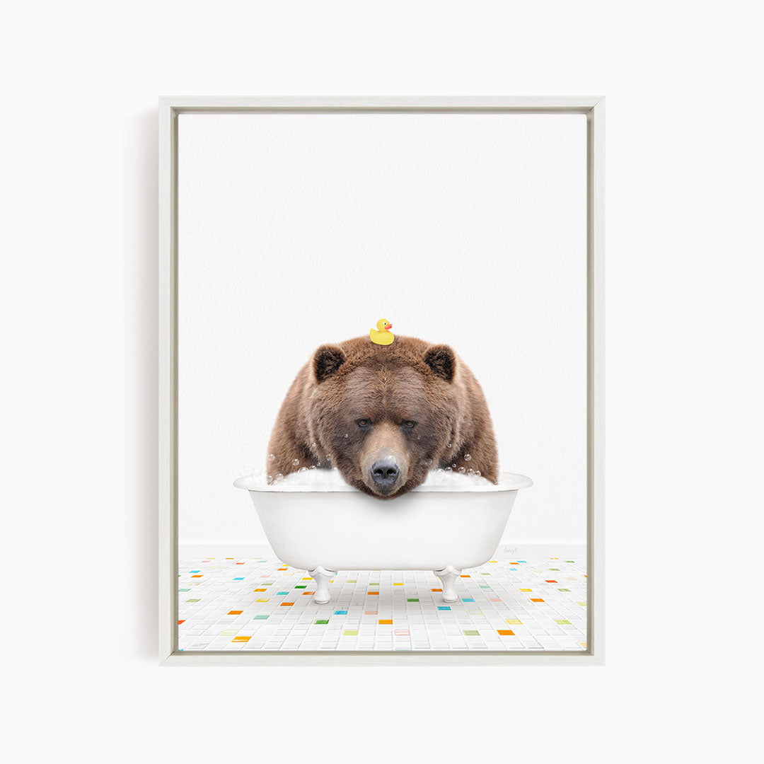 A brown bear is sitting in a white bathtub, with a yellow rubber duck perched on its head.