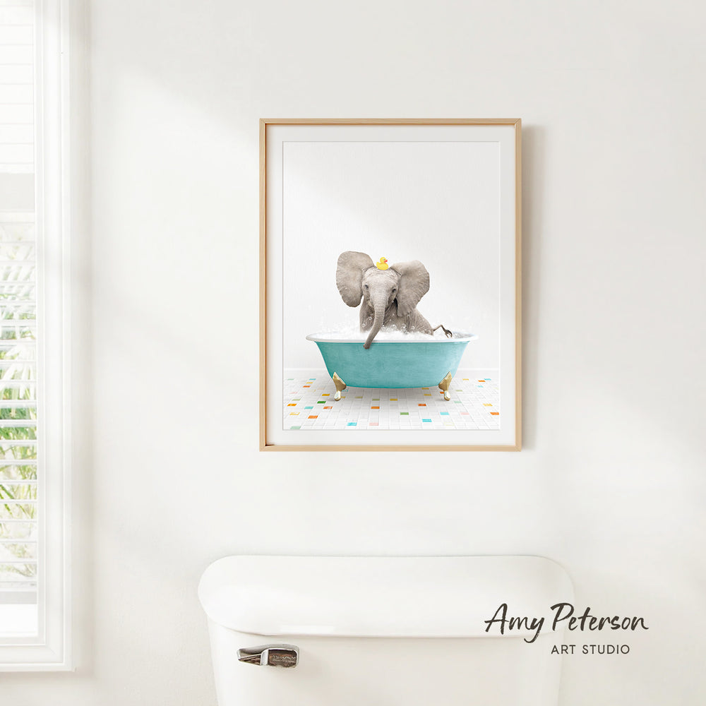 A framed image of a gray elephant sitting in a blue bathtub, with a yellow object on its head, is hanging on a white wall.