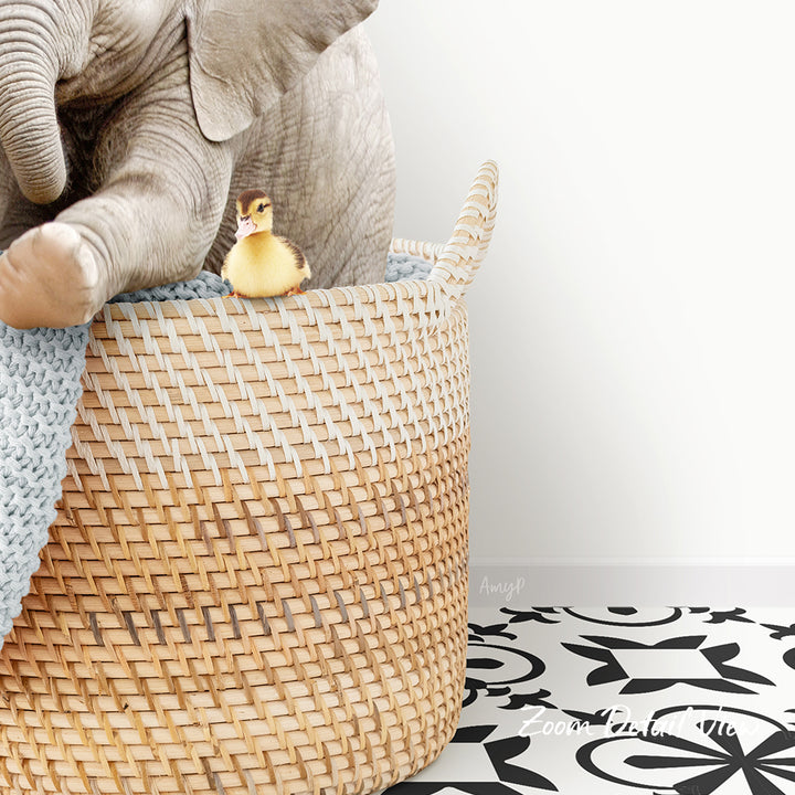 A small yellow duck sits in a woven basket, with a larger elephant trunk visible in the background.