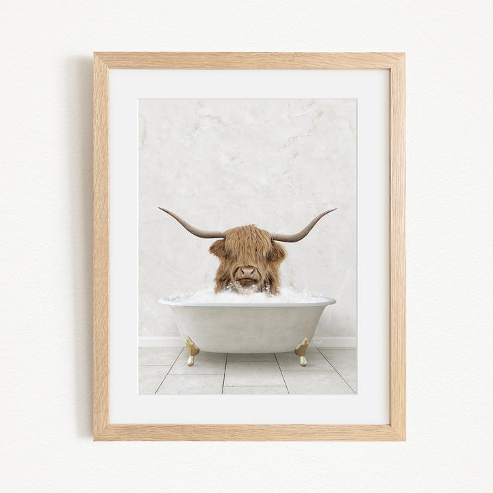 A framed image depicting a Highland cow with long horns sitting in a white bathtub filled with water.