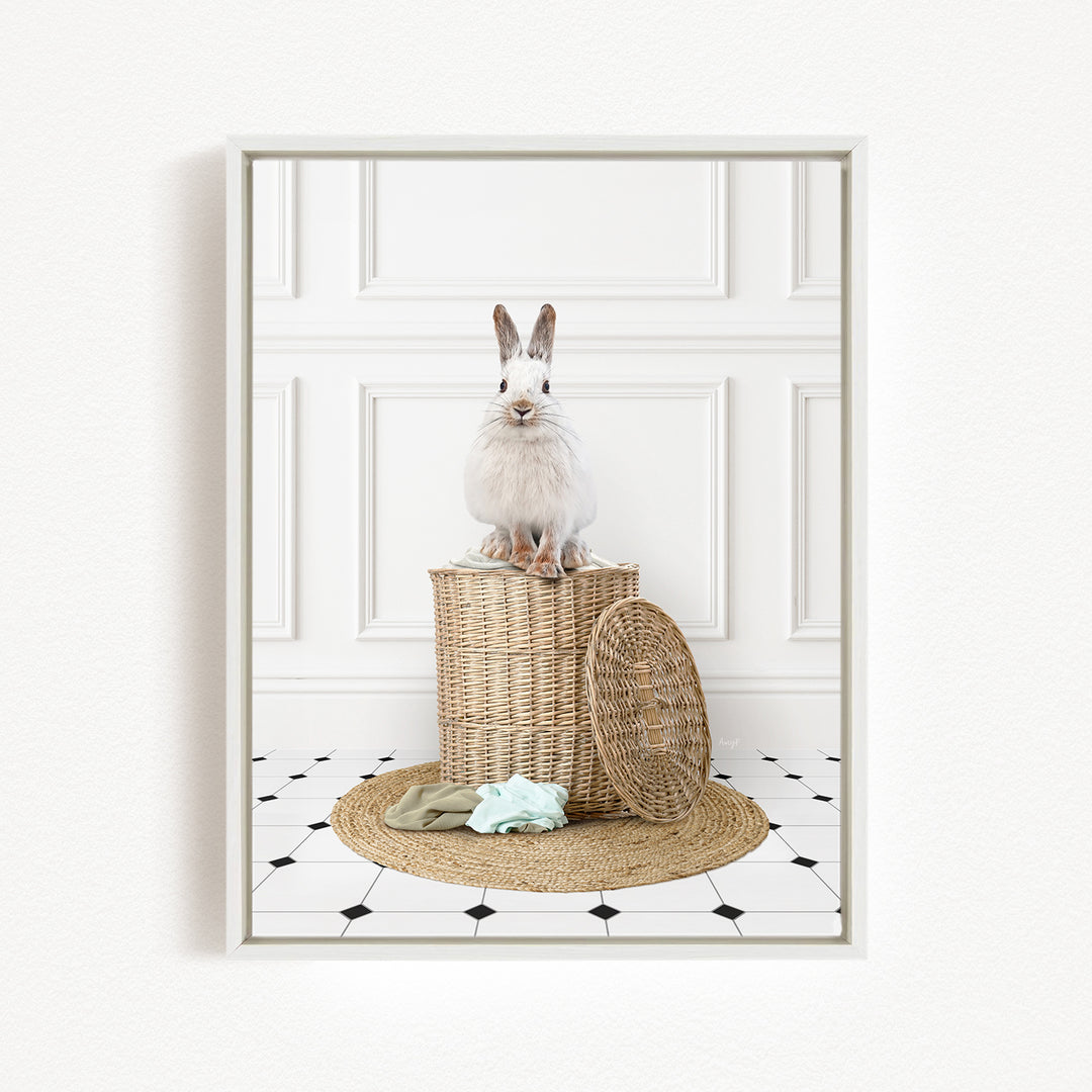 A white rabbit sits atop a woven basket on a tiled floor, with a towel and a basket lid nearby.