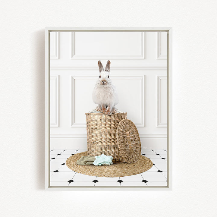 A white rabbit sits atop a woven basket on a tiled floor, with a towel and a basket lid nearby.