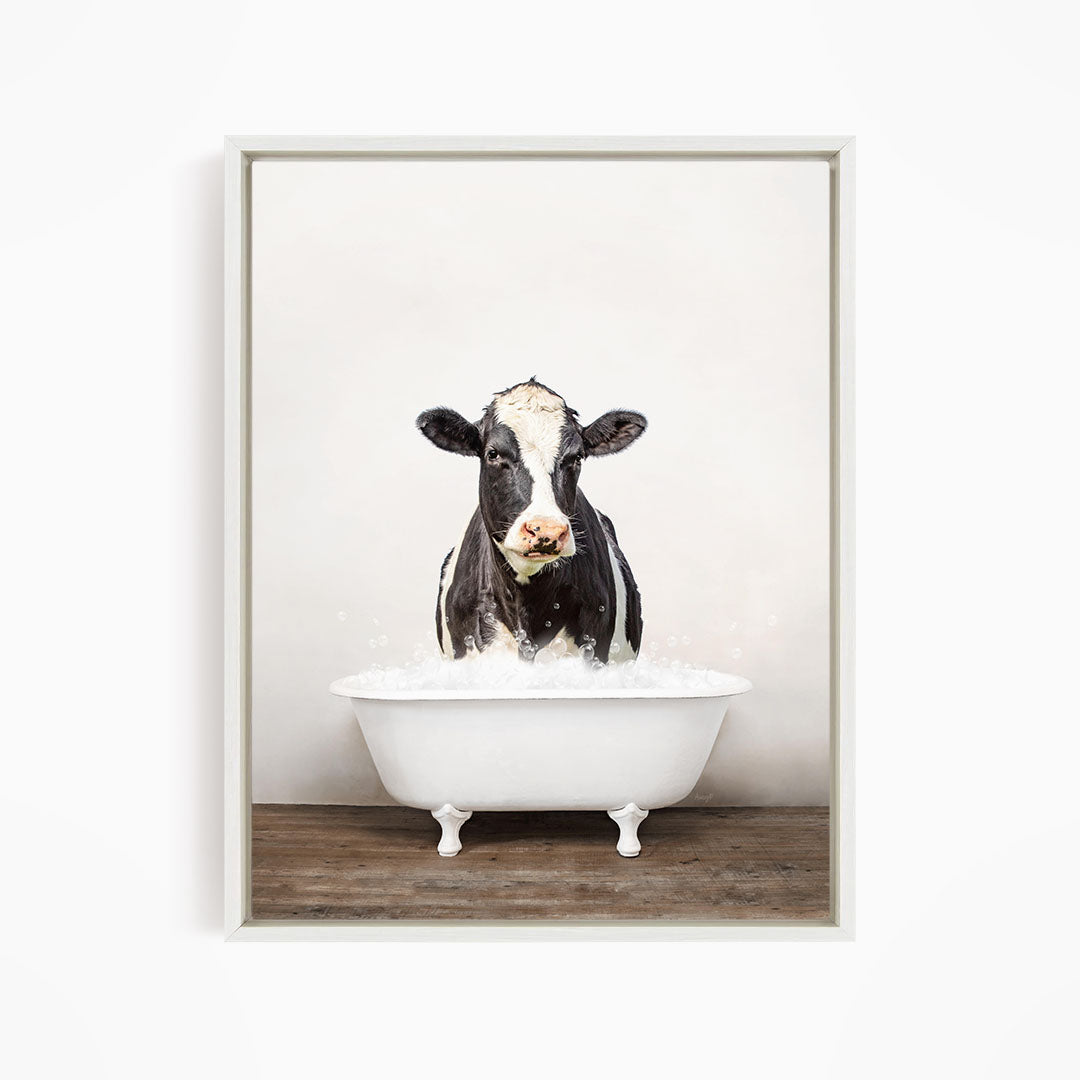 A black and white cow standing in a white bathtub filled with water, creating a whimsical and humorous scene.