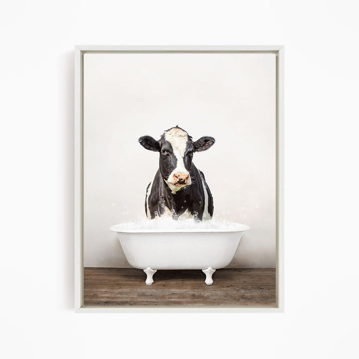 A black and white cow standing in a white bathtub filled with water, creating a whimsical and humorous scene.