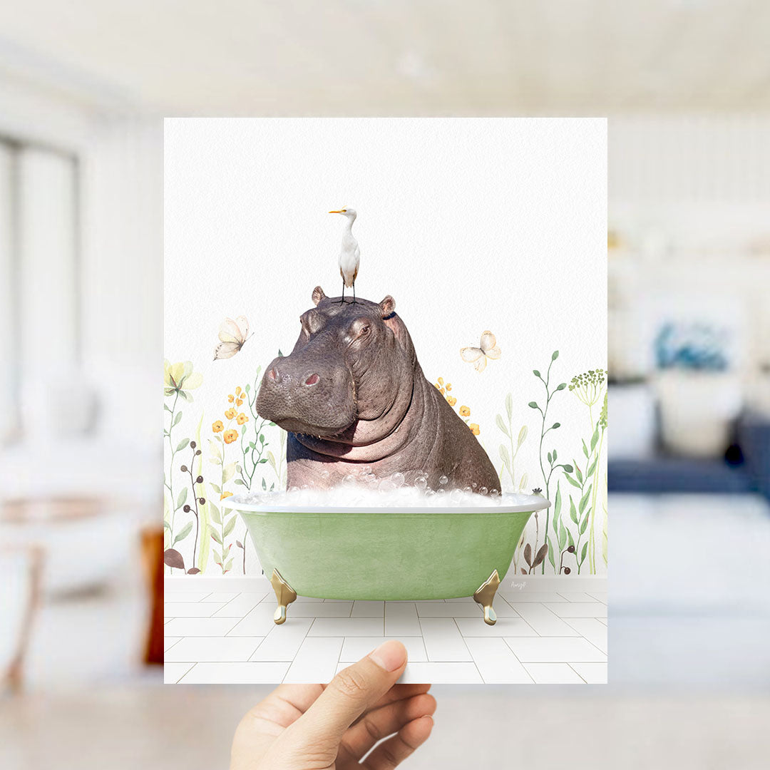 A hand holds up a framed image depicting a hippopotamus sitting in a green bathtub, with a seagull perched on its head.