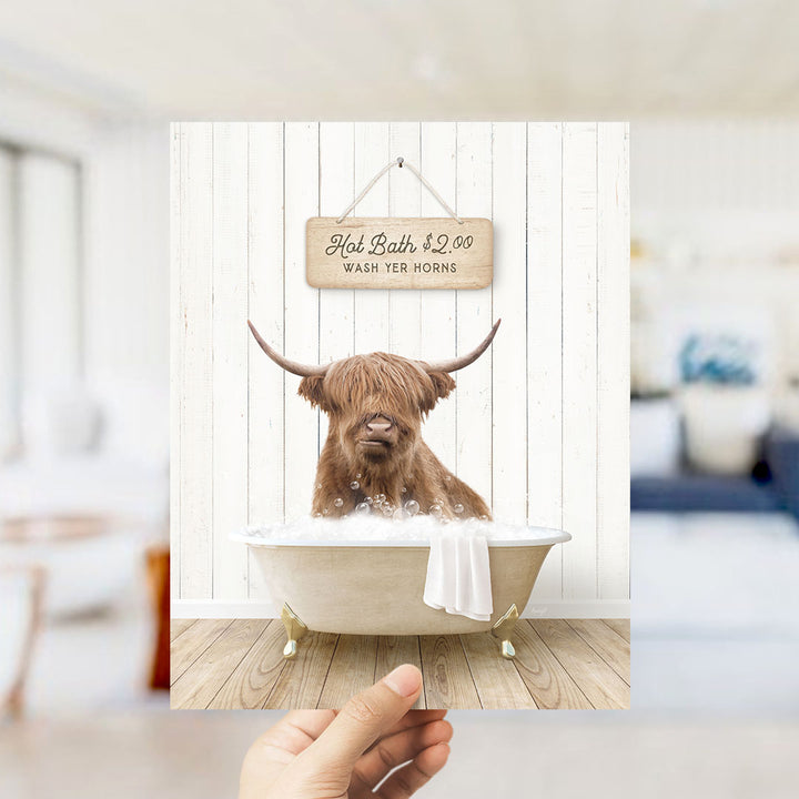 A brown Highland cow with long horns is sitting in a bathtub filled with water, with a sign above it that says "Hot Bath $2.00 Wash Your Horns".