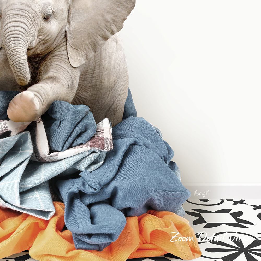 An elephant is sitting on a pile of clothes, with its trunk resting on the clothes.