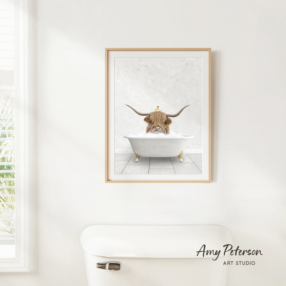 A framed image of a bull with horns sitting in a bathtub, surrounded by a white bathroom setting.