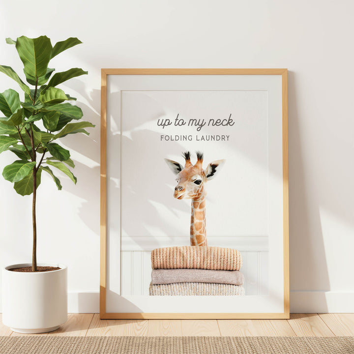 A framed image of a giraffe sitting on folded clothes, with the text "up to my neck" and "FOLDING Laundry" written above it.