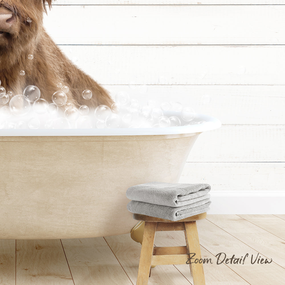 A brown dog is sitting in a bathtub filled with bubbles, with a towel and stool nearby.