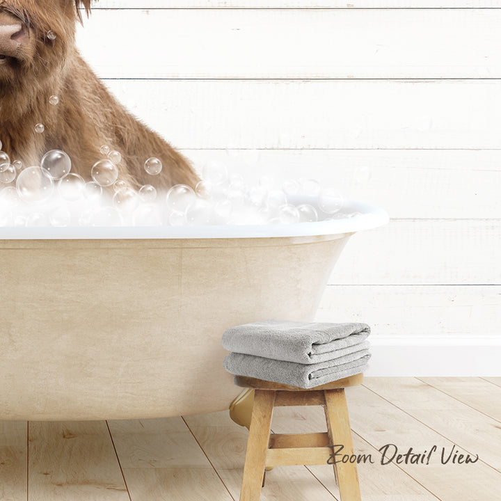 A brown dog is sitting in a bathtub filled with bubbles, with a towel and stool nearby.
