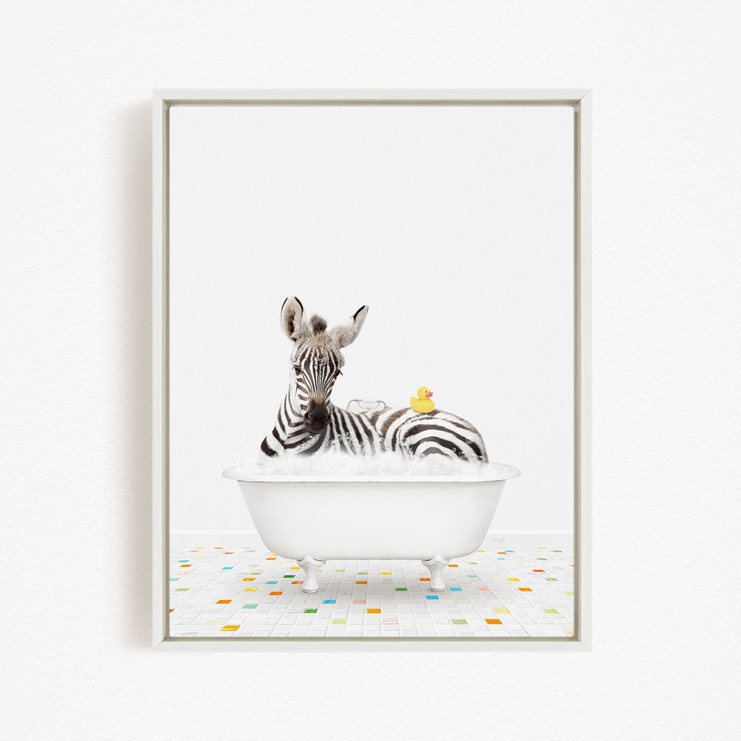 A zebra is sitting in a white bathtub filled with bubbles, with a yellow rubber duck floating on the water.