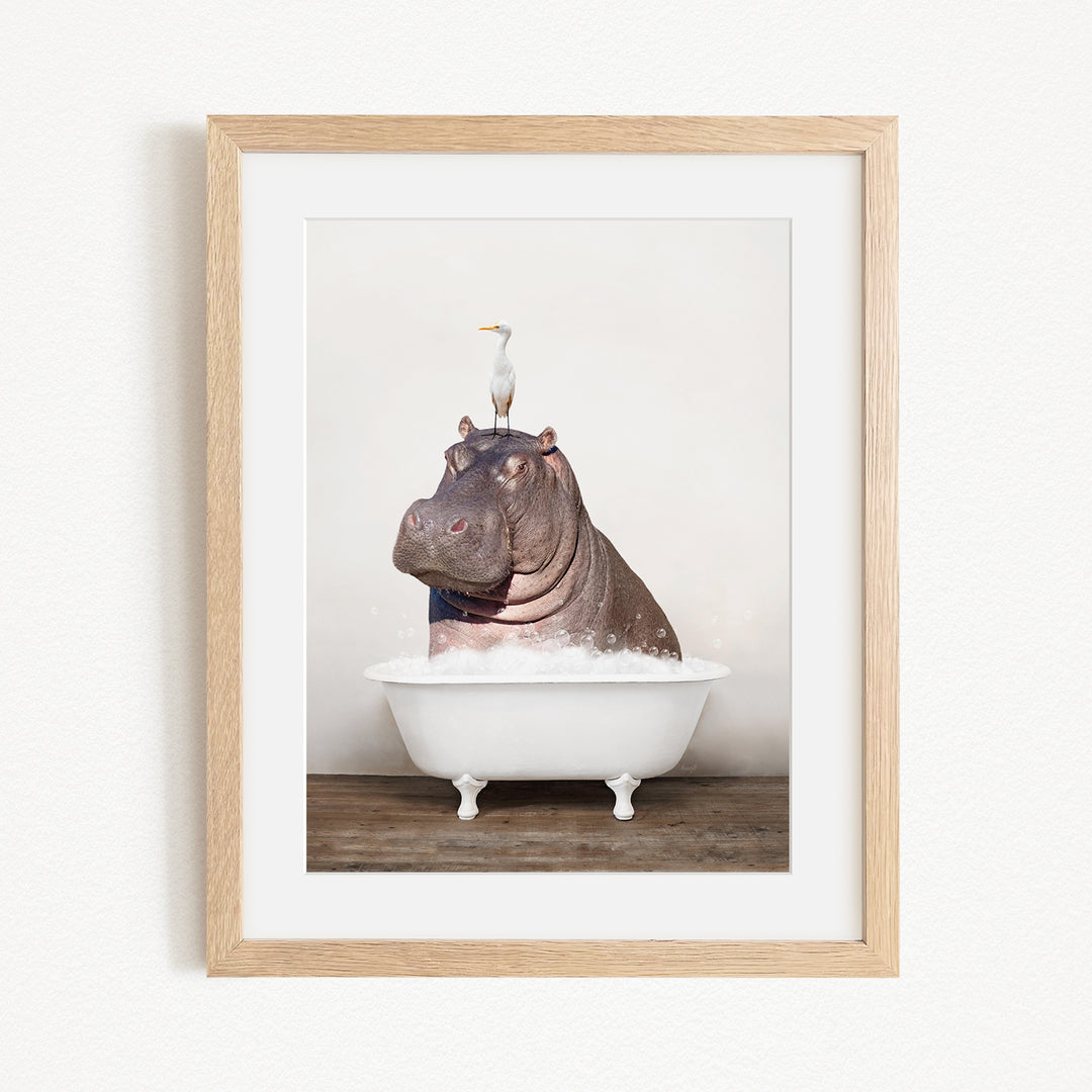 A framed image depicting a large hippopotamus sitting in a bathtub, with a seagull perched on its head.