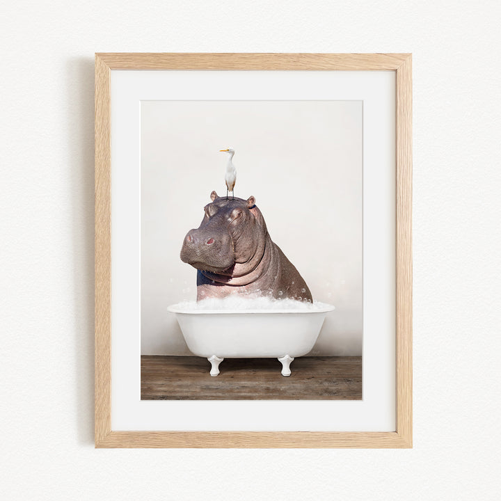 A framed image depicting a large hippopotamus sitting in a bathtub, with a seagull perched on its head.