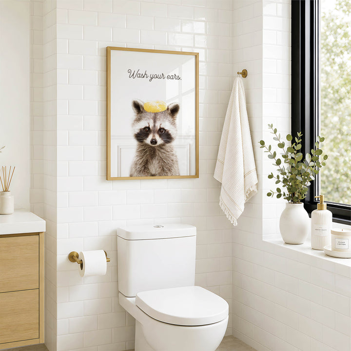 A bathroom with a white toilet, a framed raccoon image, and a towel hanging on a rack.