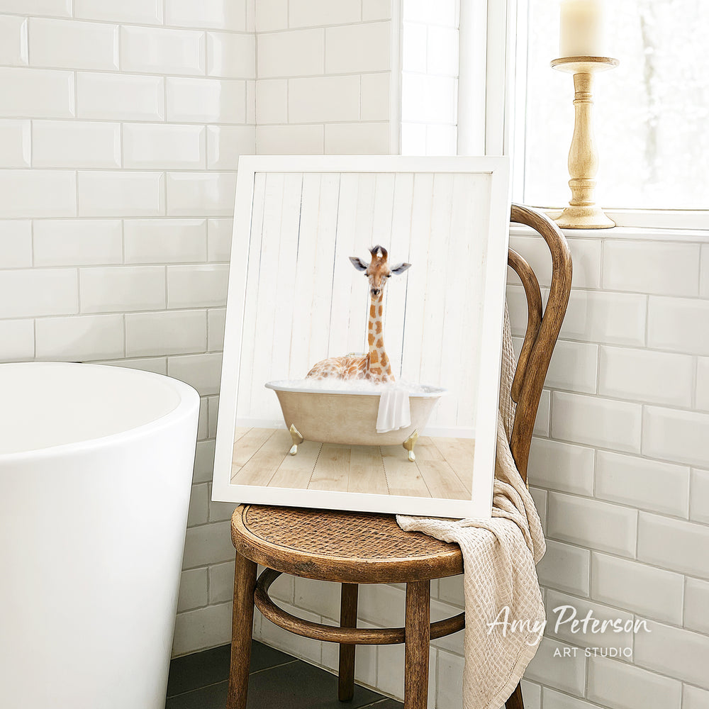 A framed image of a giraffe sitting in a bathtub, with a towel draped over the side of the tub.