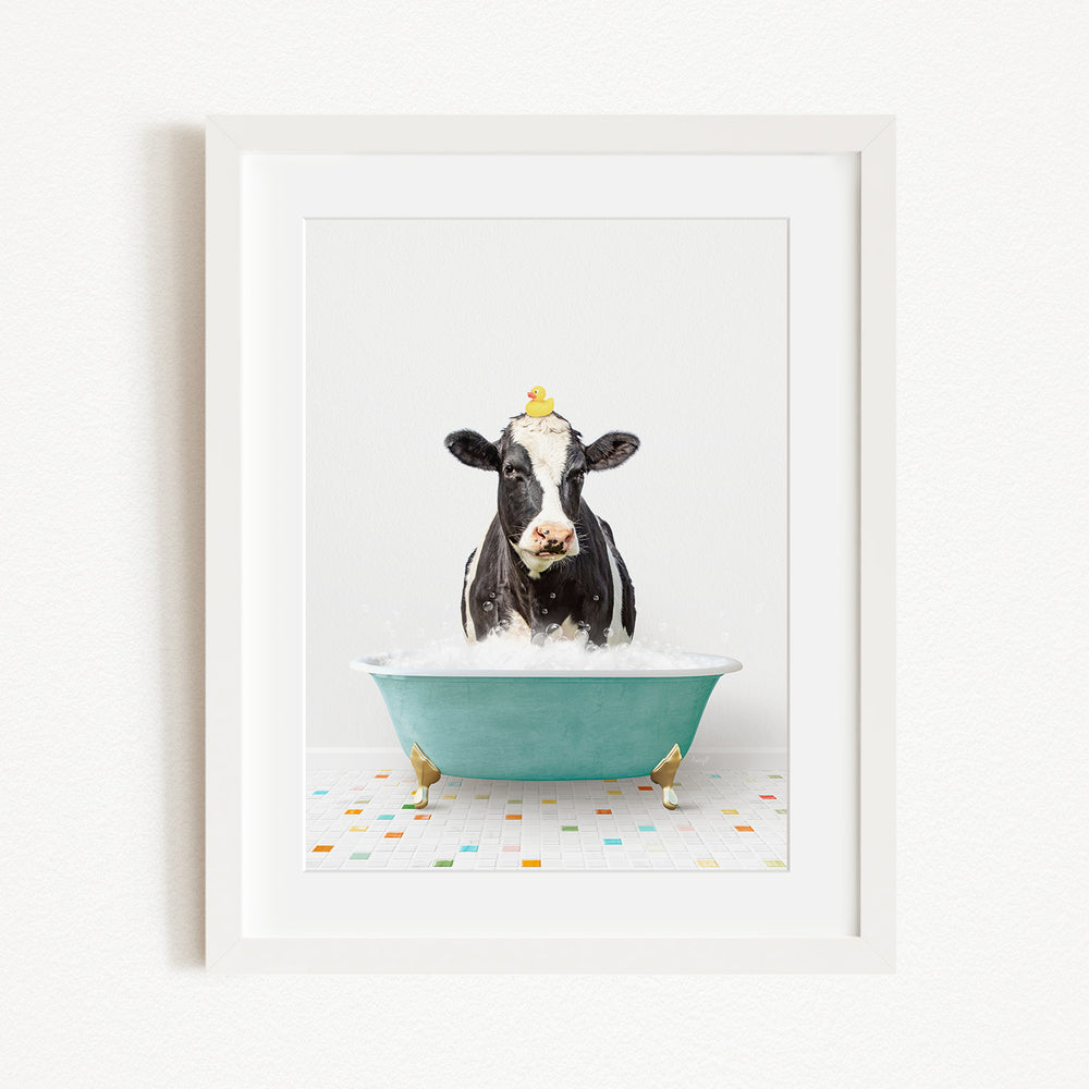 A black and white cow is sitting in a green bathtub filled with bubbles, with a yellow duck perched on its head.