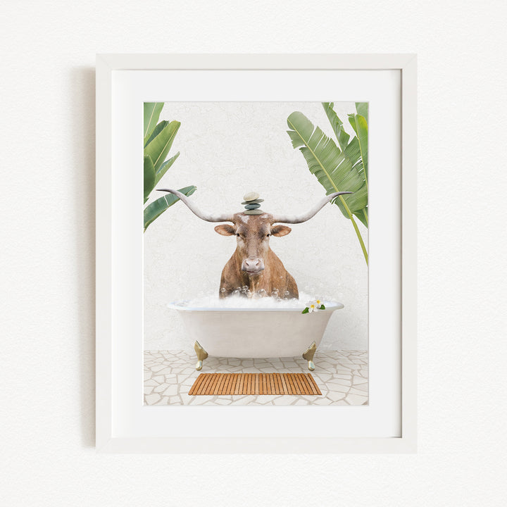 A framed image depicting a cow sitting in a bathtub filled with water, surrounded by tropical plants.