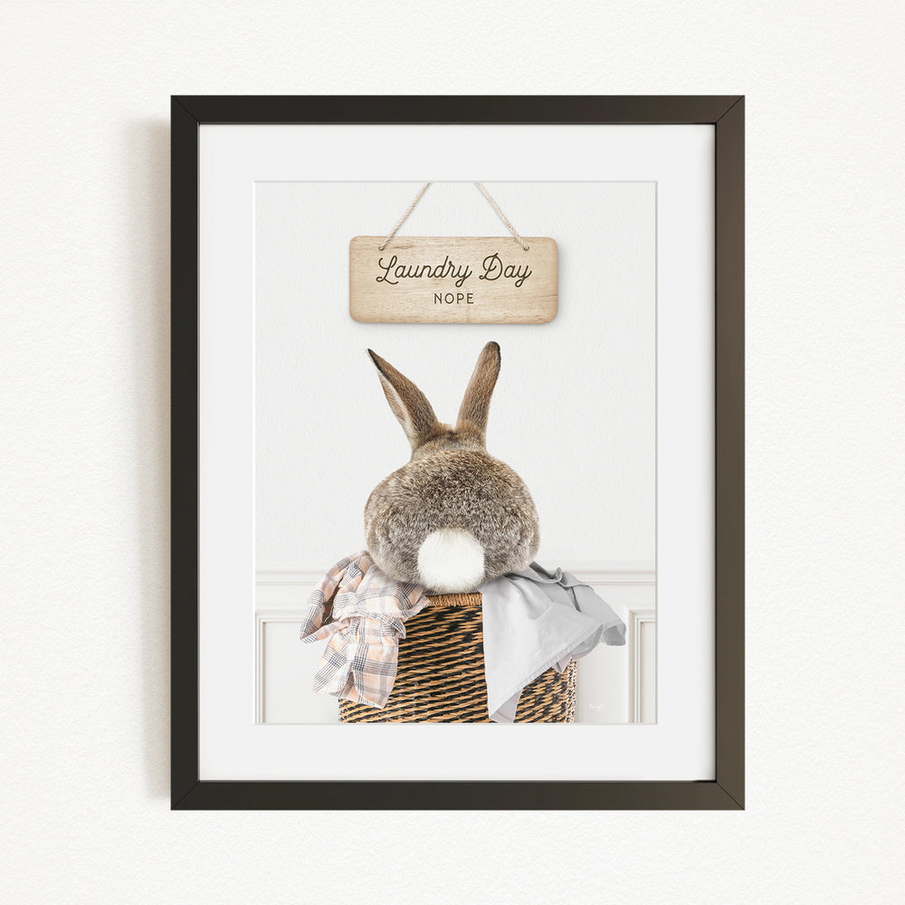 A framed image of a rabbit sitting in a basket, with a wooden sign above that says "Laundry Day".