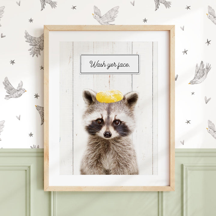 A raccoon wearing a yellow hat with the text "Wash your face" written on it, set against a white background with a pattern of birds and stars.