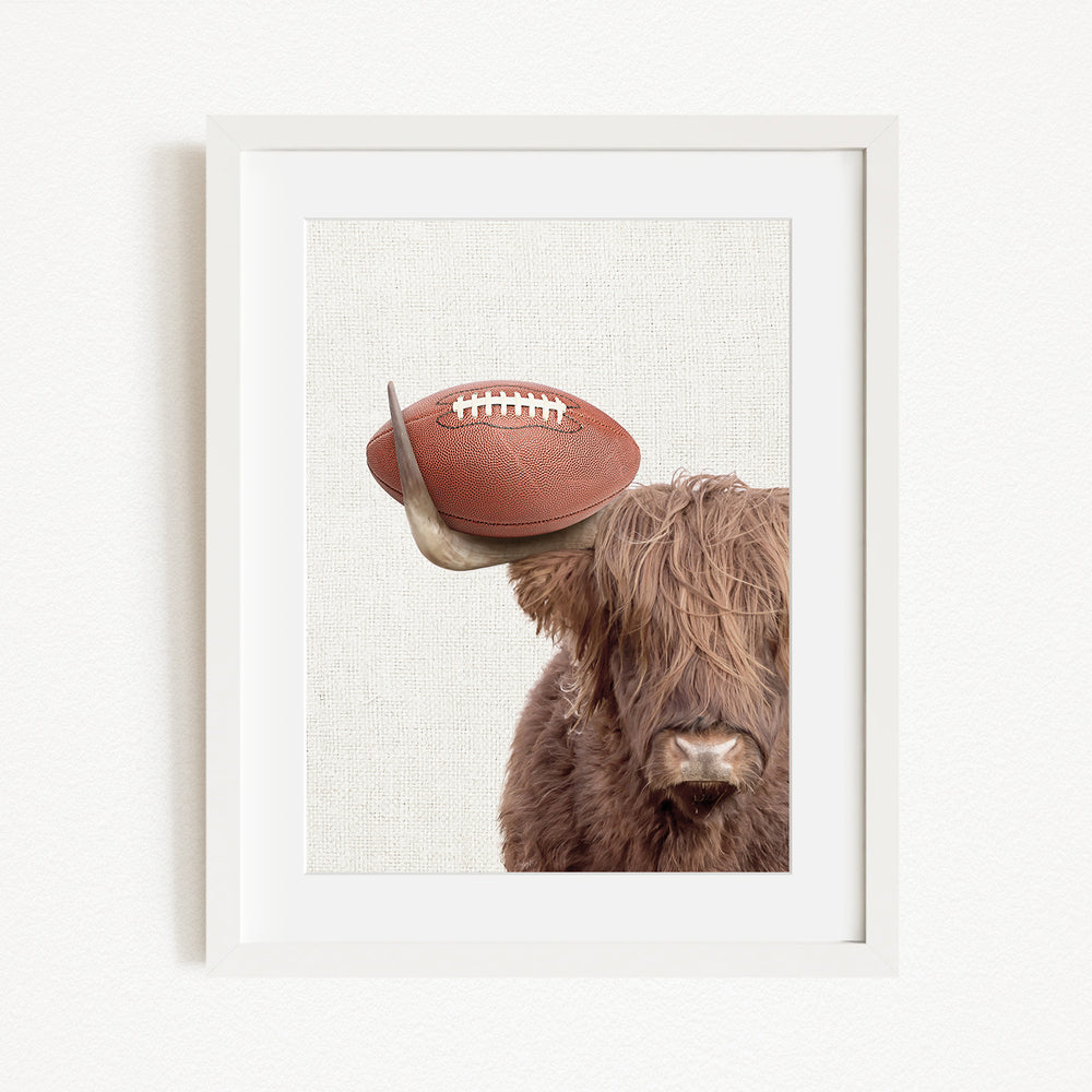 A framed image of a Highland cow with a football resting on its head.