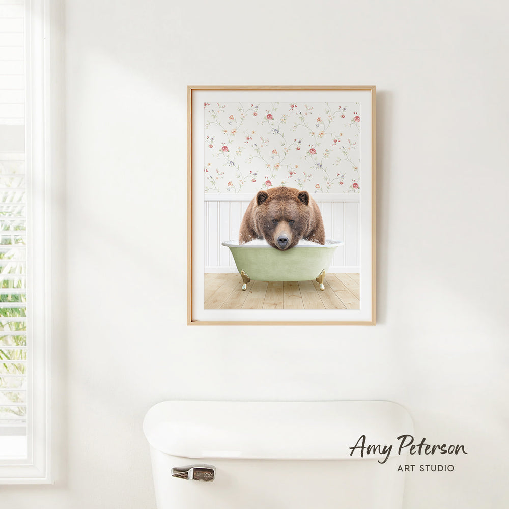 A framed image of a brown bear sitting in a bathtub, with a floral pattern on the wall behind it.