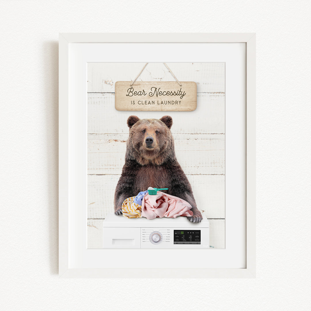 A framed image of a brown bear sitting on a washing machine, with a sign above it that says "Bear Necessity is clean laundry".