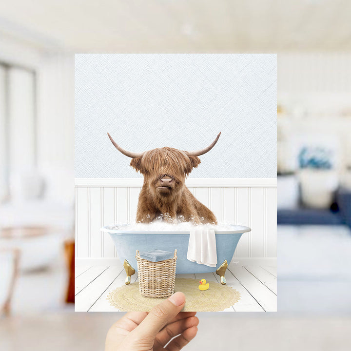 A brown cow with long horns is sitting in a blue bathtub filled with water, surrounded by a yellow rubber duck and a white towel.