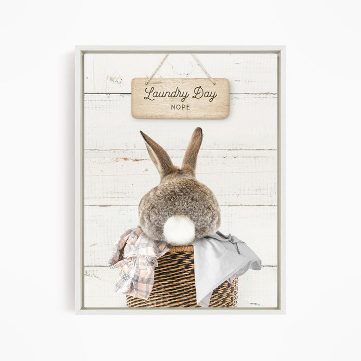 A cute rabbit sitting in a wicker basket, with a wooden sign above that says "Laundry Day NOPE".