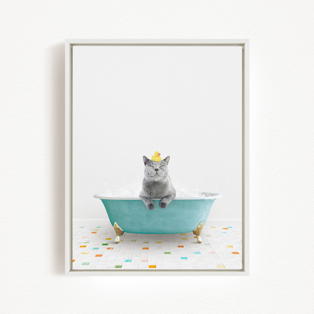 A gray cat sitting in a blue bathtub filled with bubbles, wearing a yellow rubber duck hat.