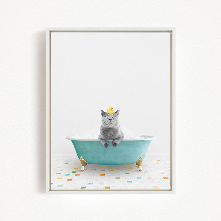 A gray cat sitting in a blue bathtub filled with bubbles, wearing a yellow rubber duck hat.
